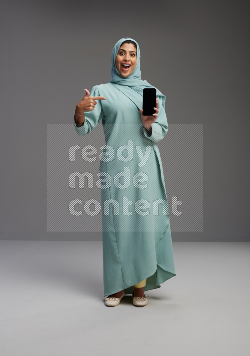 Saudi Woman wearing Abaya standing showing phone to camera on Gray background