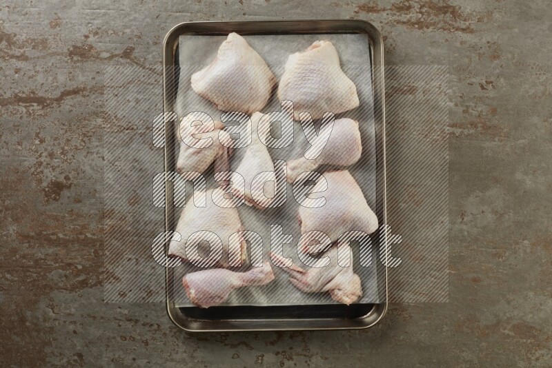 Mixed fresh chicken pieces in an oven tray on a textured rustic background