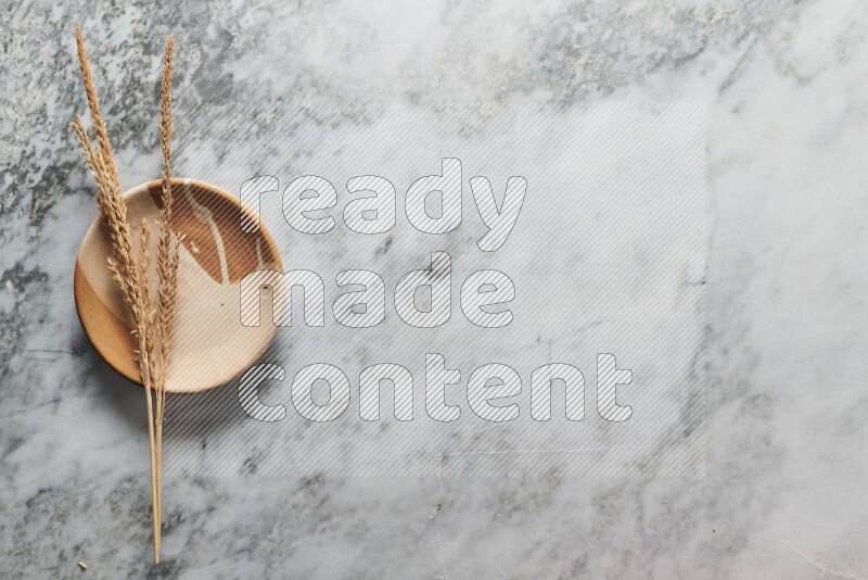 Wheat stalks on multicolored pottery plate on grey marble background