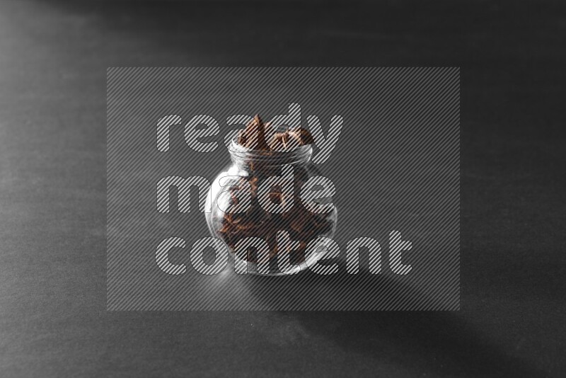 A glass spice jar full of star anise on black flooring