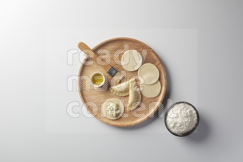 two closed sambosas and one open sambosa filled with cheese while flour, and oil with oil brush aside in a wooden dish on a white background