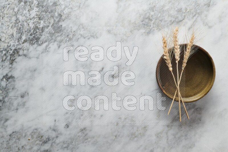 Wheat stalks on multicolored pottery oven plate on grey marble background