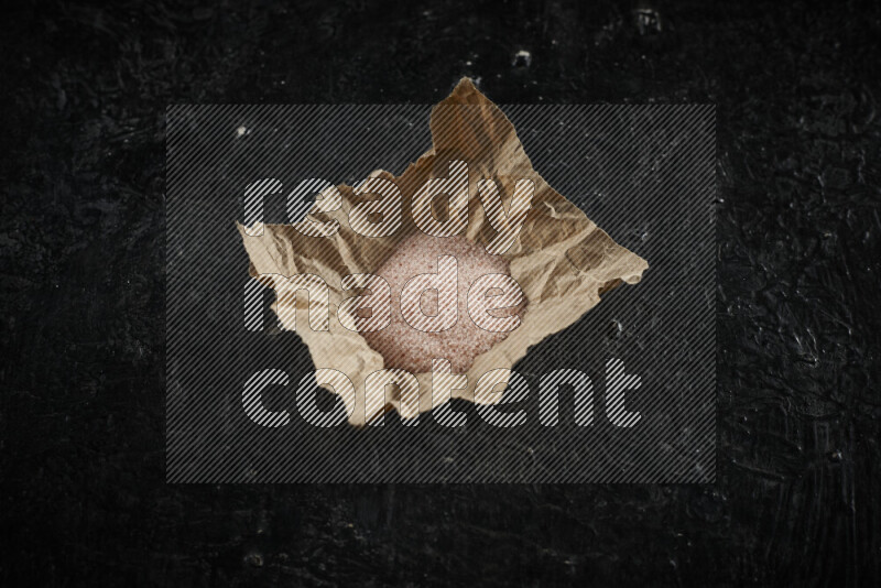 A crumpled piece of paper full of pink himalayan salt on black background