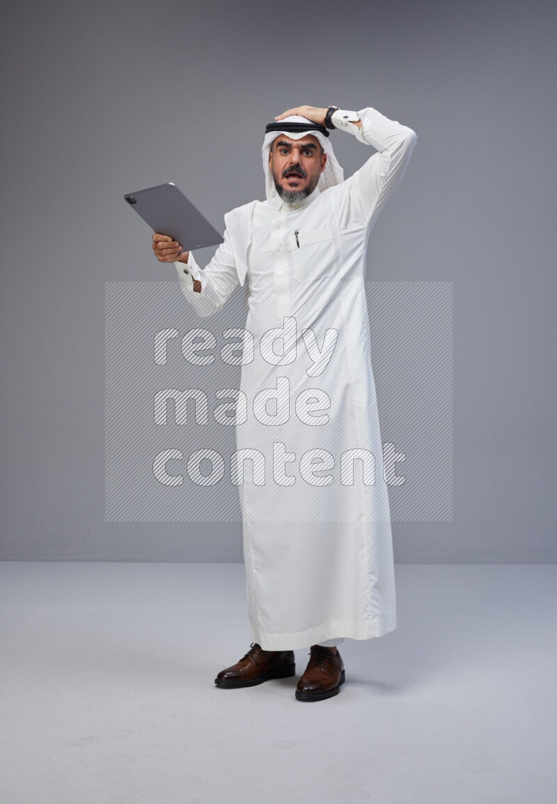 Saudi man Wearing Thob and white Shomag standing working on tablet on Gray background
