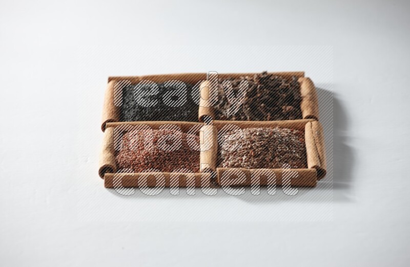 4 squares of cinnamon sticks full of black seeds, cloves, flaxseeds and garden cress on white flooring