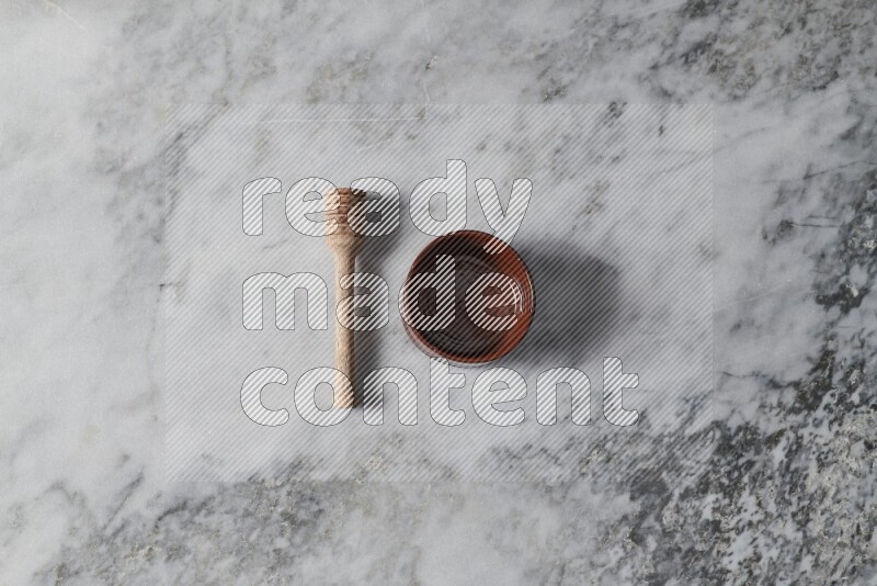Brown pottery bowl with wooden honey dipper on the side on grey marble background