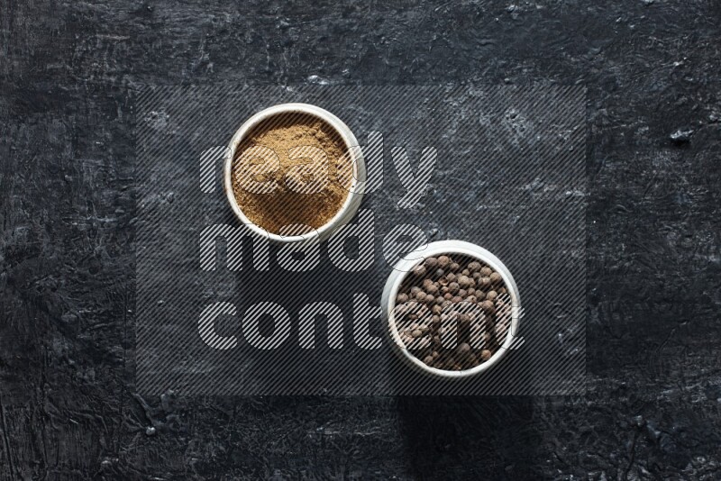 2 beige bowls, one full of allspice powder and the other full of whole balls on a textured black flooring