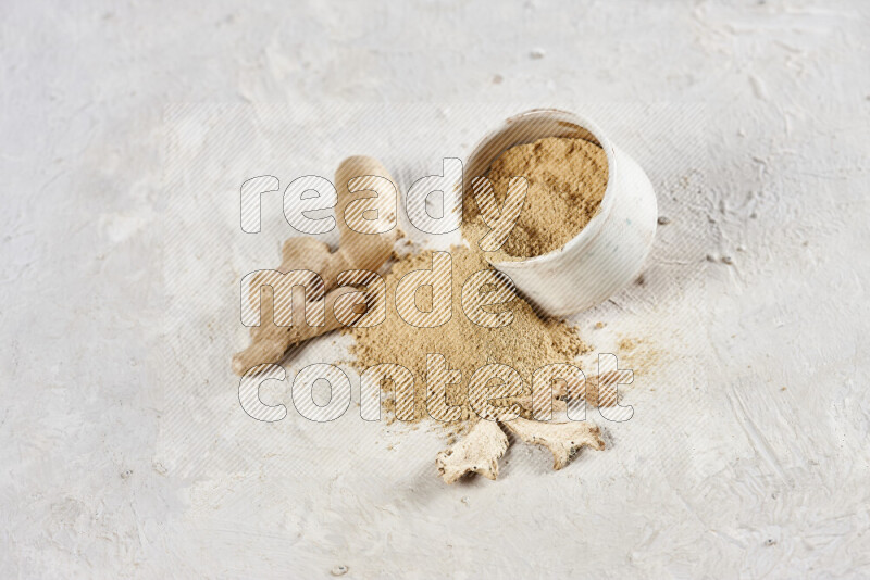 A beige pottery bowl full of ground ginger powder with fallen powder from it on white background