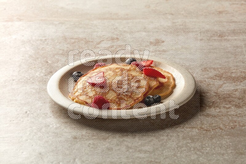 Three stacked mixed berries pancakes in a grey plate on beige background