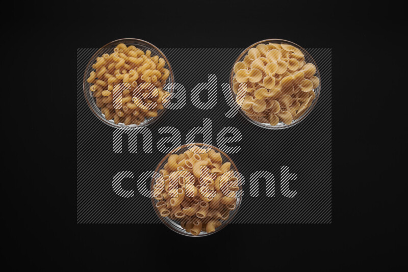 Different pasta types in glass bowls on black background