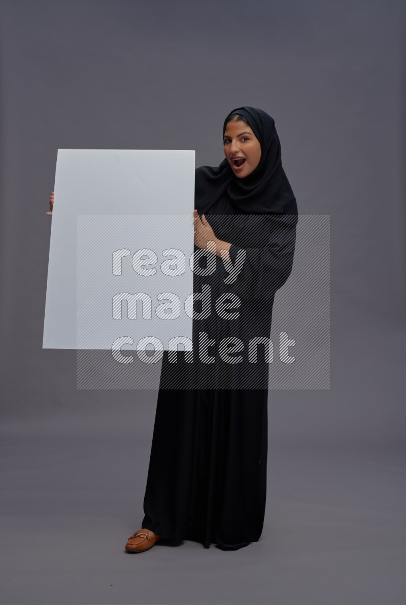 Saudi woman wearing Abaya standing holding white board on gray background