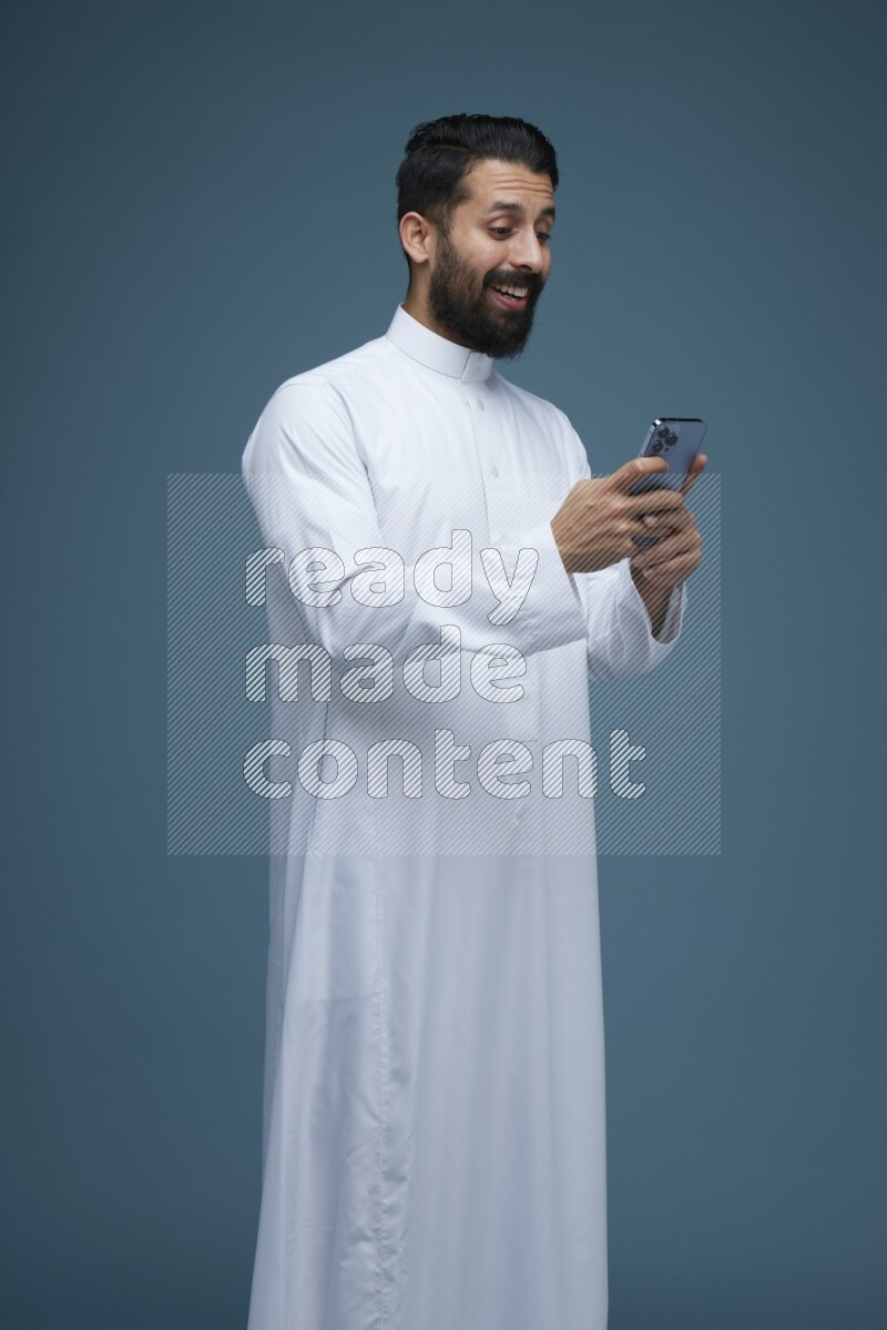 A man Texting in a blue background wearing Saudi Thob