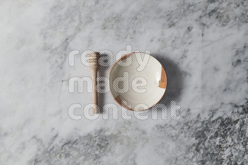 Multicolored pottery plate with wooden honey dipper on the side on grey marble background