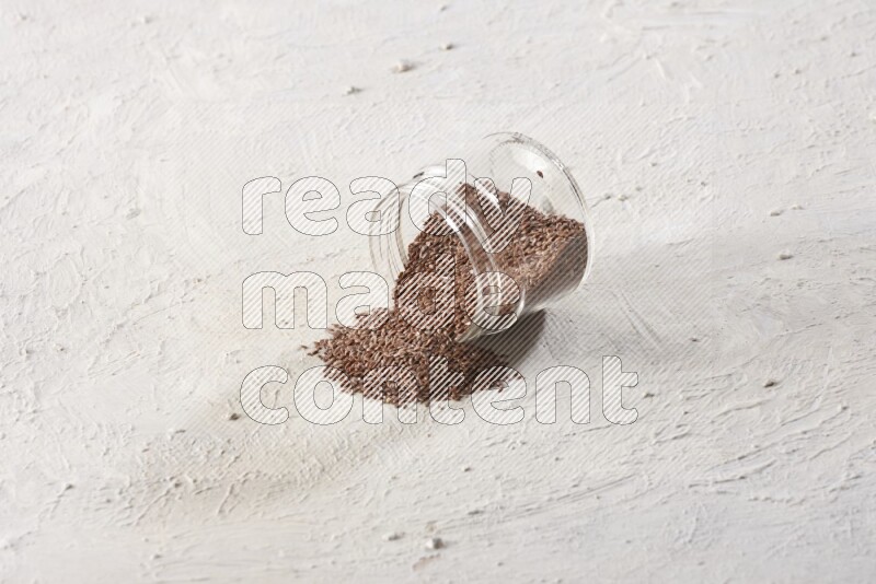 A glass jar full of flax seeds flipped and seeds spread out on a textured white flooring