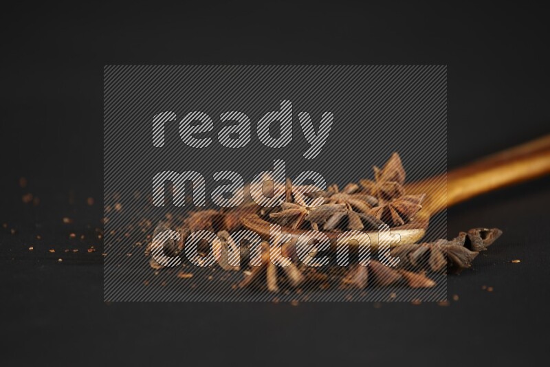 يانسون نجمي في مغرفة خشبية مع المزيد من اليانسون على خلفية سوداء