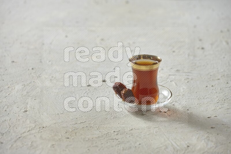 A tea glass cup with dates and coffee on textured white background
