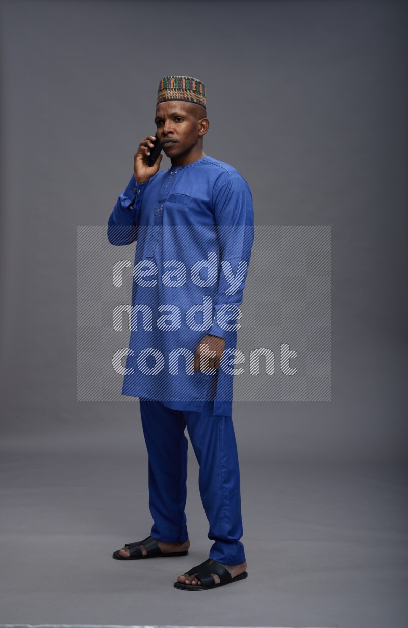 Man wearing Nigerian outfit standing talking on phone on gray background