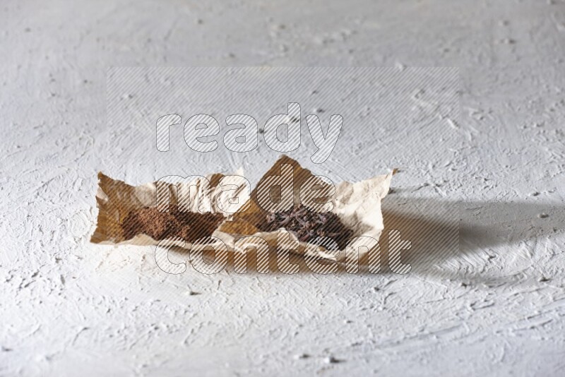 Cloves powder and cloves on 2 crumpled pieces of paper on a textured white flooring