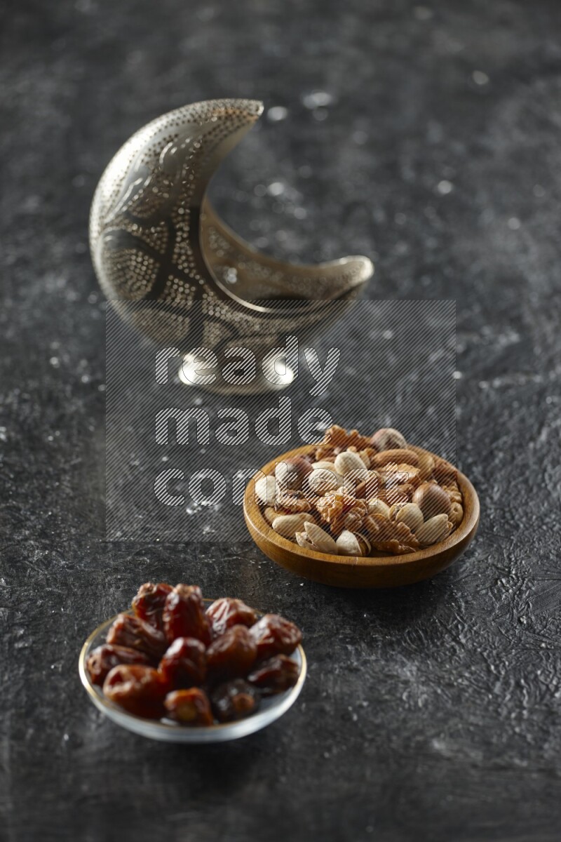 A silver lantern with different drinks, dates, nuts, prayer beads and quran on textured black background