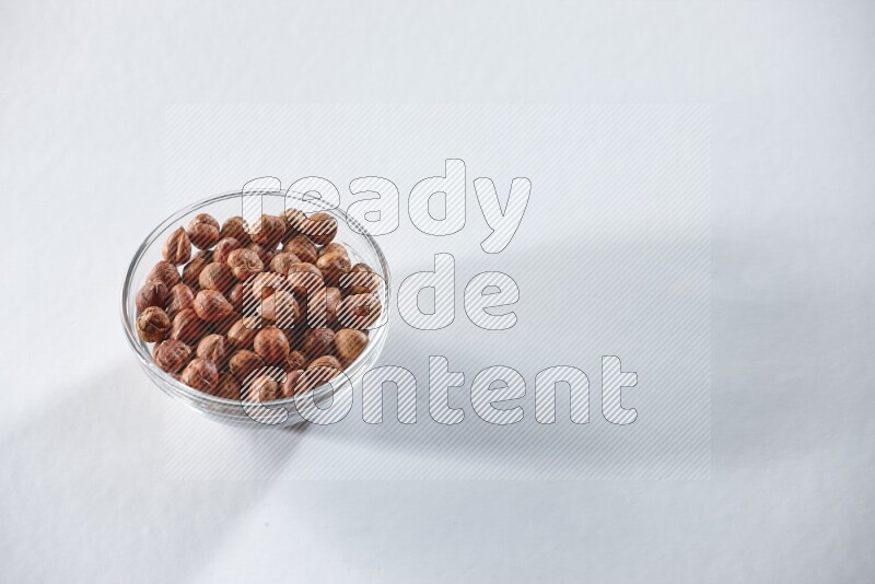 A glass bowl full of peeled hazelnuts on a white background in different angles