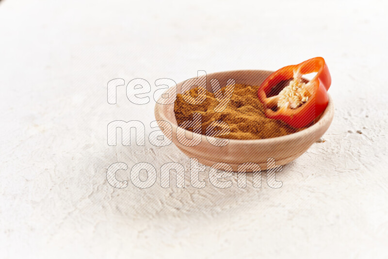 A wooden bowl full of ground paprika powder on white background