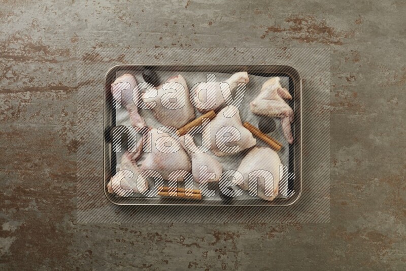 Mixed fresh chicken pieces in an oven tray on a textured rustic background