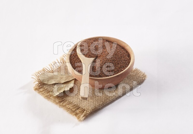 A wooden bowl and spoon full of garden cress seeds on burlap fabric on a white flooring