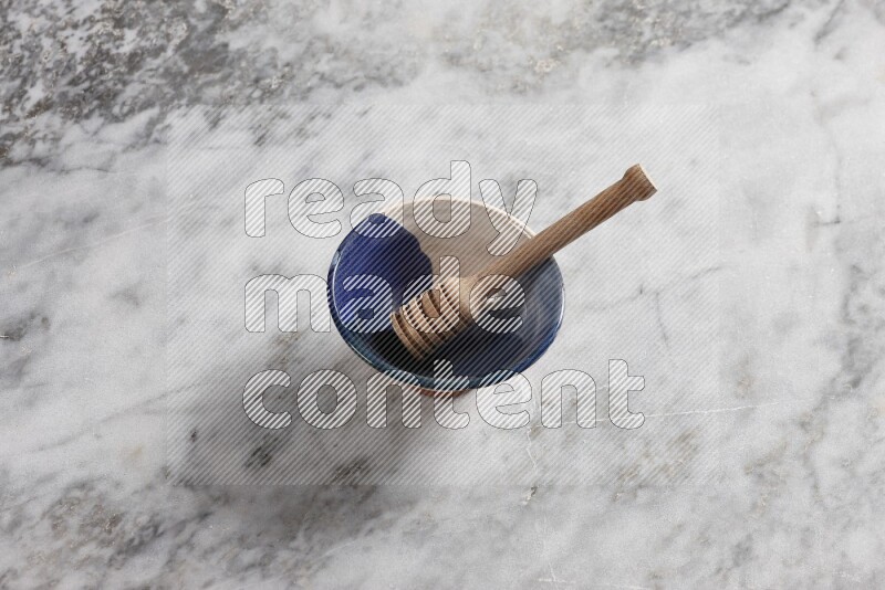 Multicolored pottery bowl with wooden honey dipper in it on grey marble background