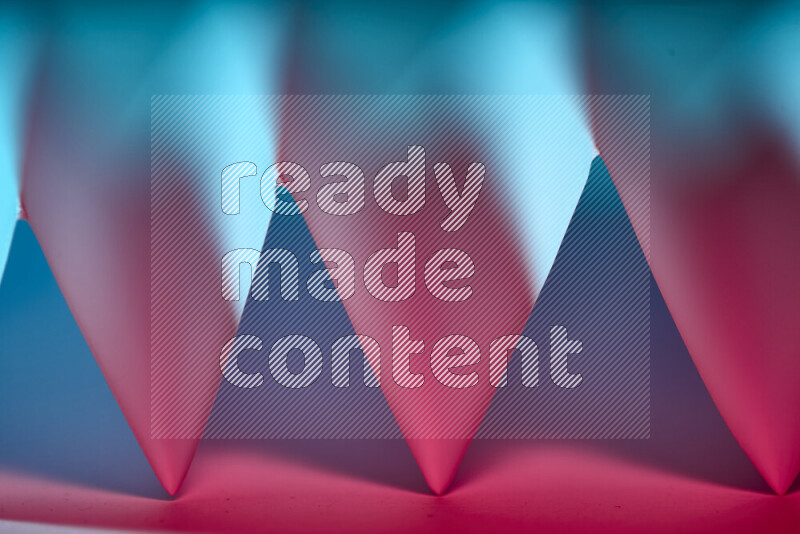 A close-up abstract image showing sharp geometric paper folds in blue and red gradients