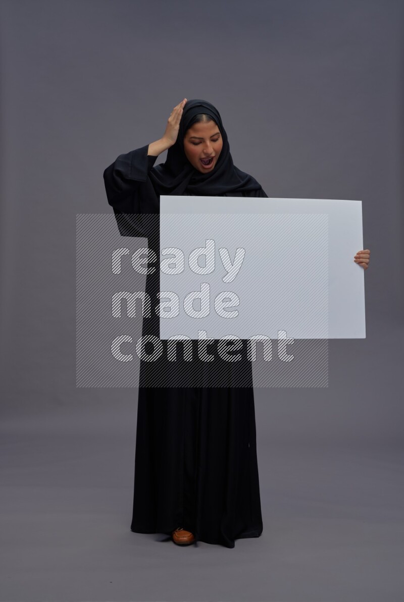 Saudi woman wearing Abaya standing holding white board on gray background