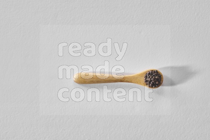 A wooden spoon full of black pepper on white flooring
