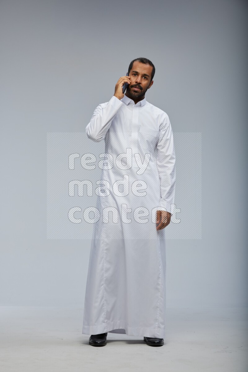 Saudi man wearing Thob standing talking on phone on Gray background
