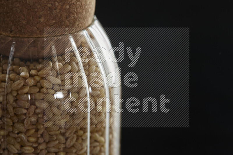 Hulled wheat in a glass jar on black background