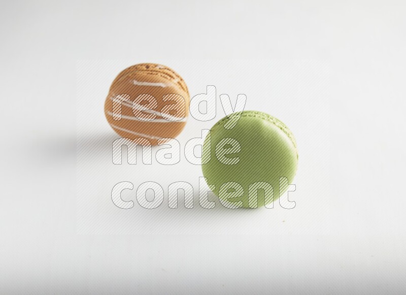 45º Shot of of two assorted Brown Irish Cream, and Green Pistachio macarons on white background