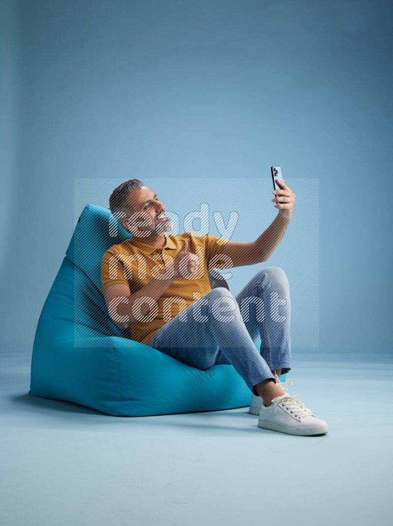 A man sitting on a blue beanbag and taking selfie