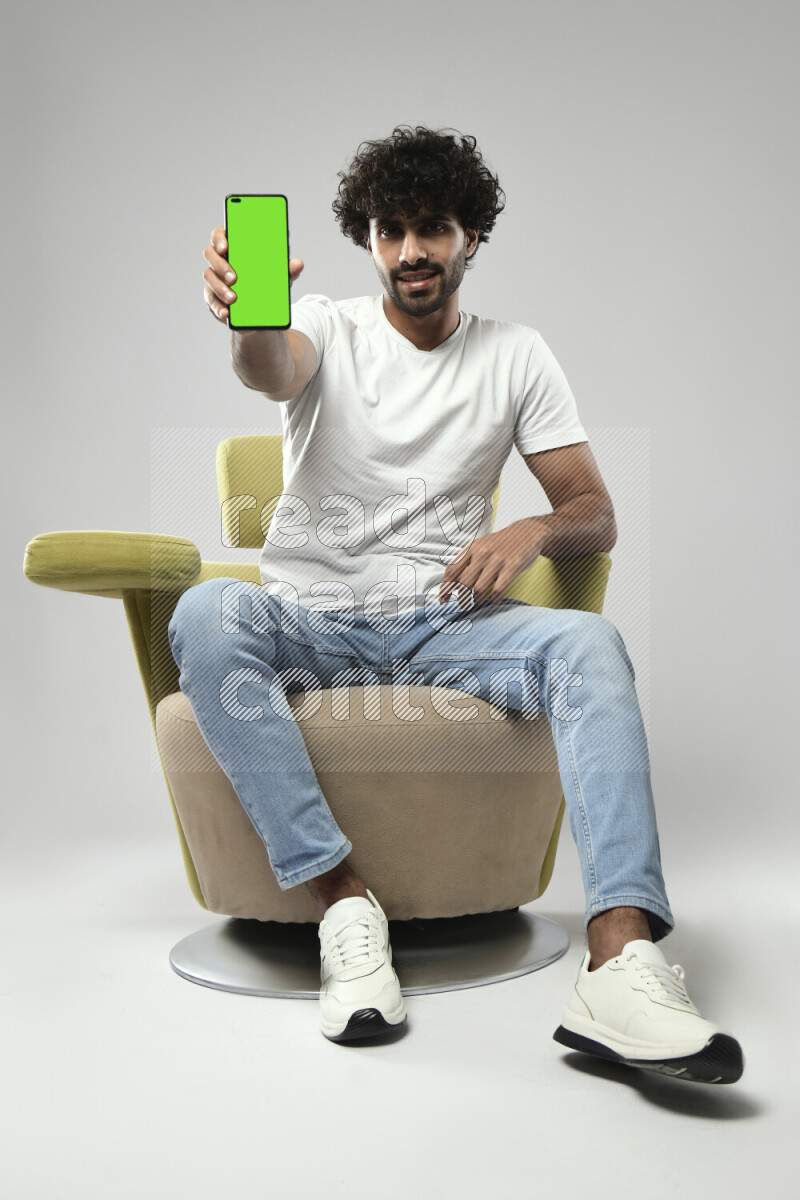 A man wearing casual sitting on a chair showing a phone screen on white background