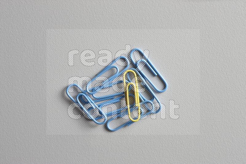 A bunch of blue paper clips with a different colored paper clip in the center on grey background