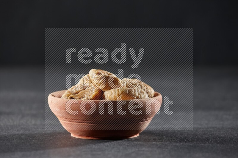 A wooden bowl full of dried figs on a black background in different angles