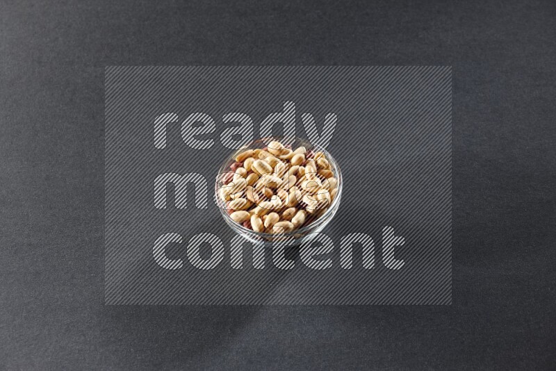 A glass bowl full of peeled peanuts on a black background in different angles