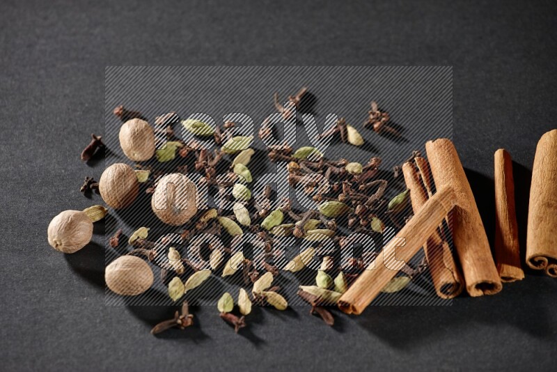 Cardamom, cloves, nutmeg and cinnamon sticks on black flooring