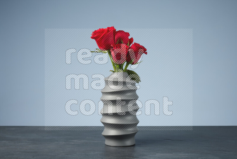 An arrangement of vivid red roses in a grey spiral vase on black marble background