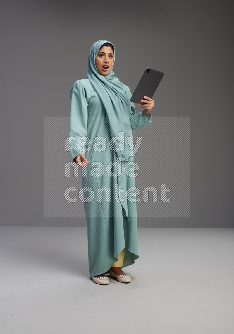 Saudi Woman wearing Abaya standing working on tablet on Gray background