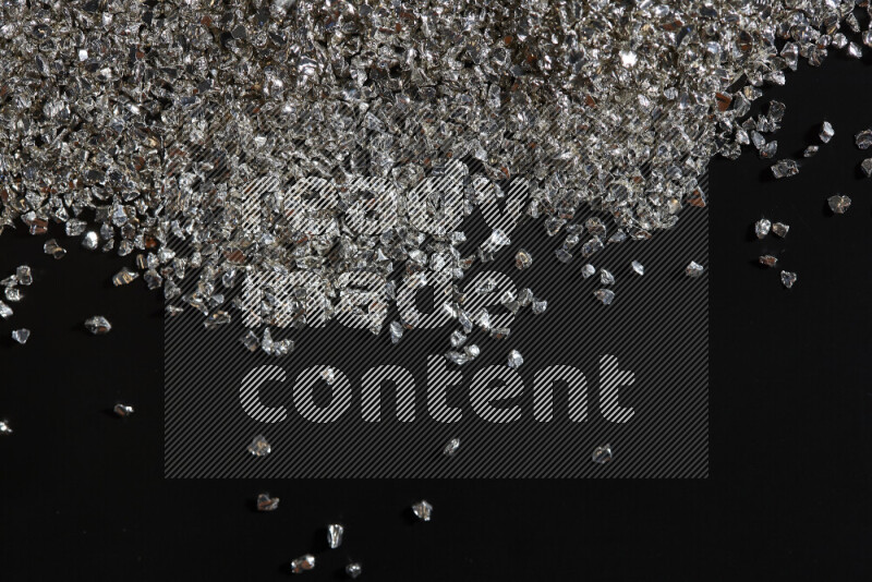 Silver shimmering fragments of glass scattered on a black background