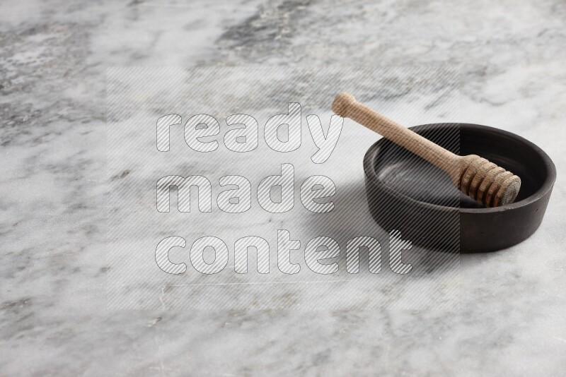 Black pottery oven plate with wooden honey dipper in it on grey marble background