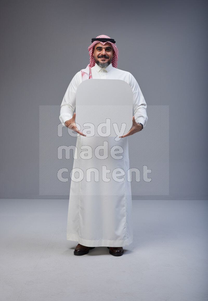 Saudi man Wearing Thob and red Shomag standing holding social media sign on Gray background