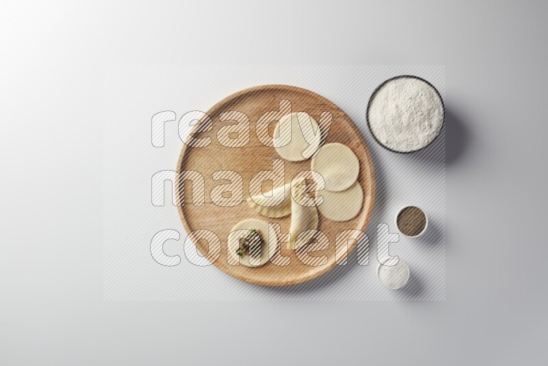 two closed sambosas and one open sambosa filled with meat while flour, salt, and black pepper aside in a wooden dish on a white background