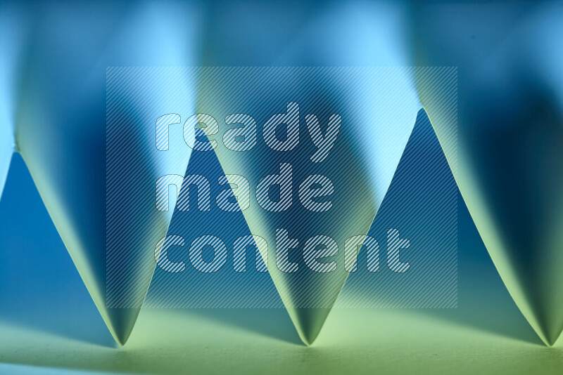 A close-up abstract image showing sharp geometric paper folds in green and blue gradients