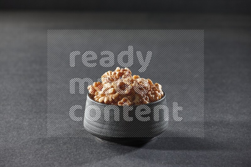A black pottery bowl full of peeled walnuts on a black background in different angles