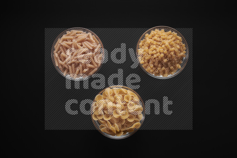 Different pasta types in glass bowls on black background