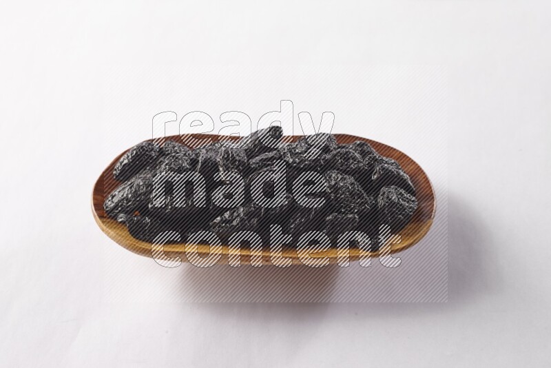 Dried plums in a wooden plate on white background